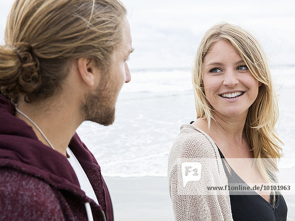 Young man and young woman on a beach  looking at each other  smiling.