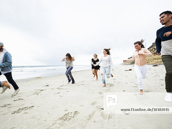A group of young men and women running on a beach  having fun.