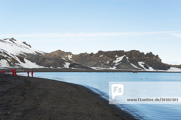 Group of people on a beach on Deception Island  snow-covered mountains in the background.
