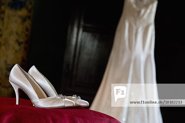 Weiße Satinhochhackige Hochzeitsschuhe mit hohen Absätzen und ein Kleid zum Aufhängen.