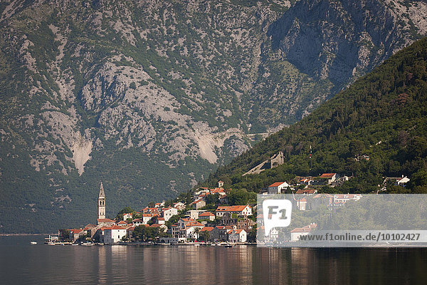 Blick über einen See auf ein Dorf an den Hängen eines Berges in Montenegro.