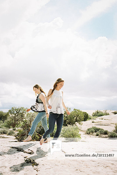 Two women running barefoot across the sand in a desert landscape
