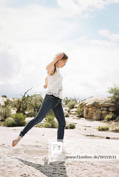 A woman wearing jeans dancing barefoot in the desert.
