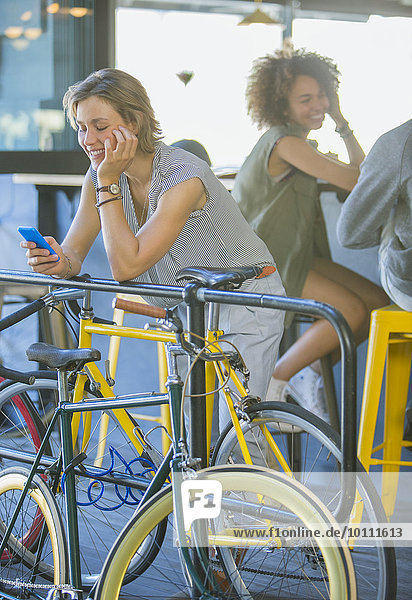 Smiling woman leaning on railing texting with cell phone above bicycle