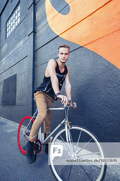 Porträt eines ernsthaften jungen Mannes auf dem Fahrrad neben der städtischen Graffiti-Wand