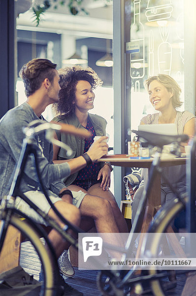 Freunde,  die hinter dem Fahrrad am Kaffeetisch sitzen