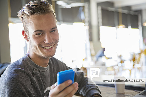 Portrait smiling young man texting with cell phone in cafe