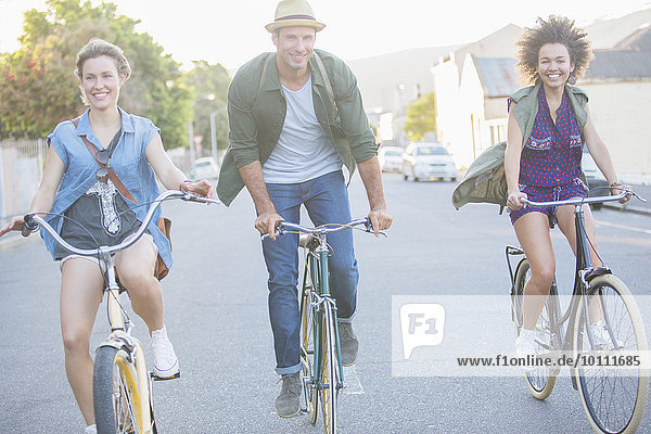 Smiling friends riding bicycles on street