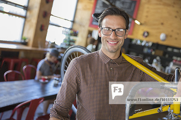 Portrait smiling man with eyeglasses carrying bicycle in cafe