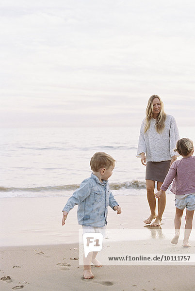 Woman playing with her son and daughter on a sandy beach by the ocean.
