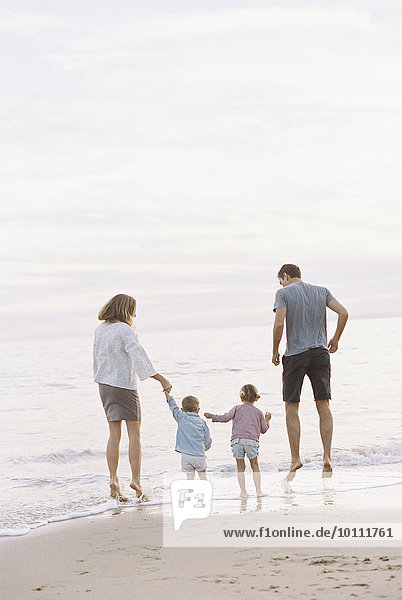Couple playing with their son and daughter on a sandy beach by the ocean  holding hands.