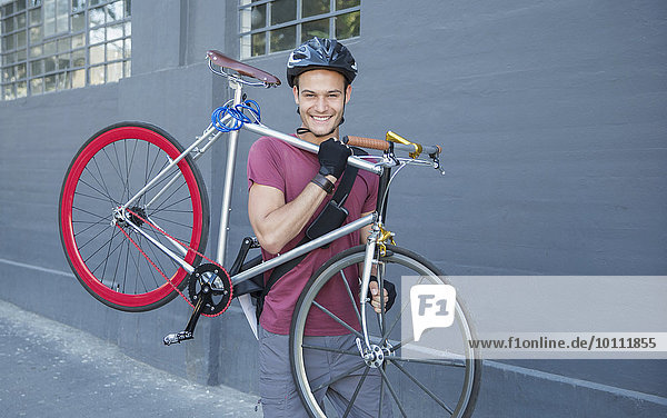 Portrait smiling young man carrying bicycle on urban sidewalk