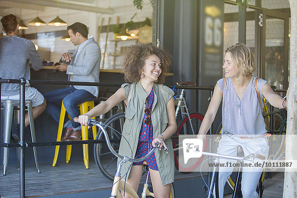 Lächelnde Frauen auf Fahrrädern vor der Café-Terrasse