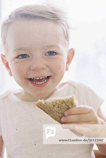Portrait of a smiling young boy eating a sandwich.
