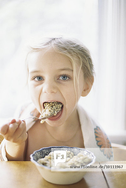 Young girl sitting at a table  eating breakfast from a bowl.