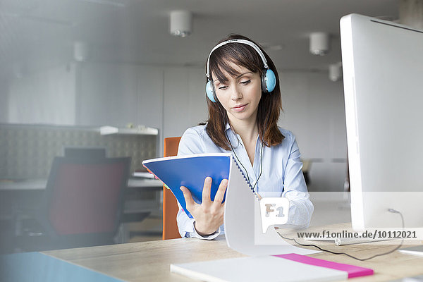 Geschäftsfrau mit Kopfhörer Lesebericht am Computer im Büro