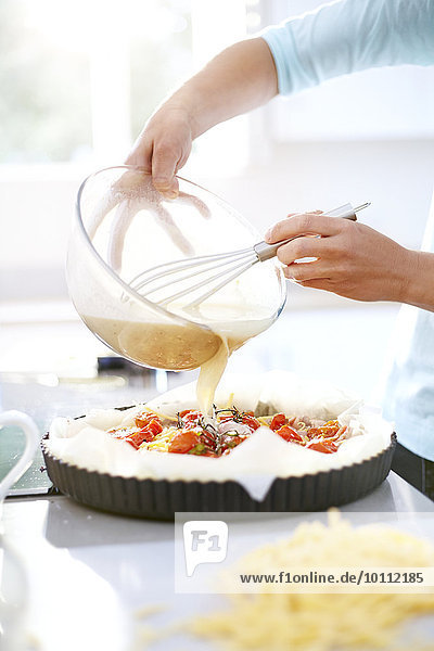 Woman preparing tomato quiche in kitchen