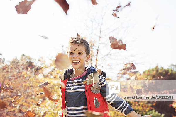 Portrait of enthusiastic boy throwing autumn leaves