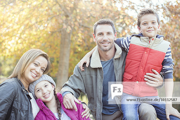 Portrait smiling family in front of tree with autumn leaves