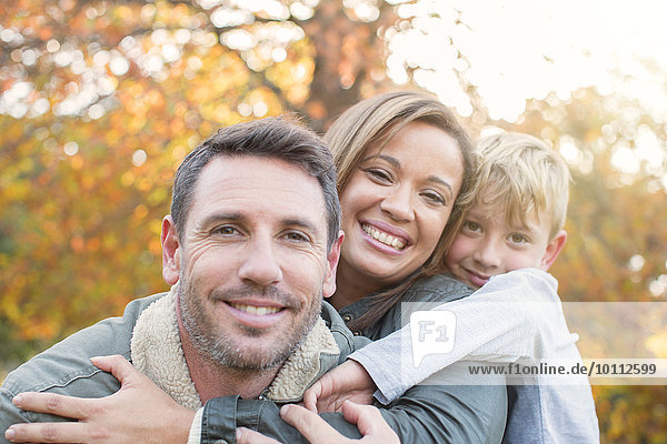 Portrait smiling family hugging in front of autumn leaves