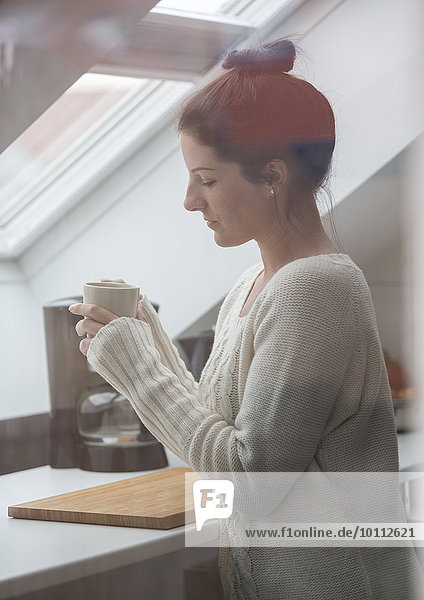 Dunkelhaarige Frau mit Kaffeetasse in Mansardenwohnung