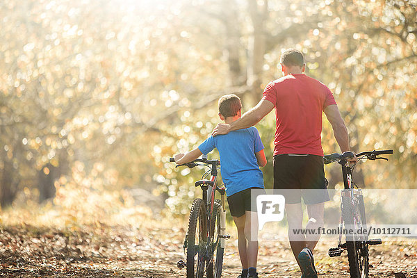 Affectionate father and son walking mountain bikes on path in woods
