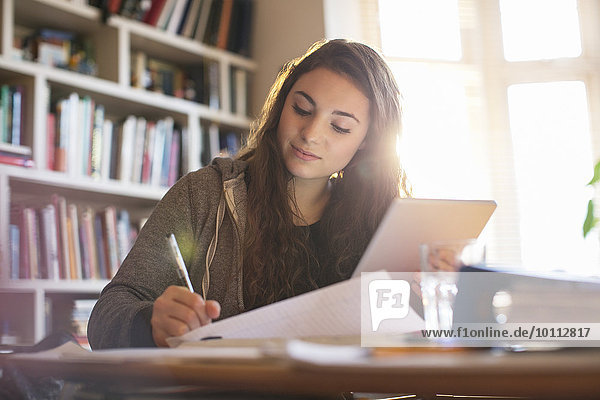 Teenage girl with digital tablet doing homework at desk