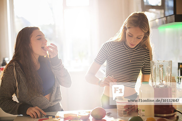 Teenage girls making smoothie in sunny kitchen