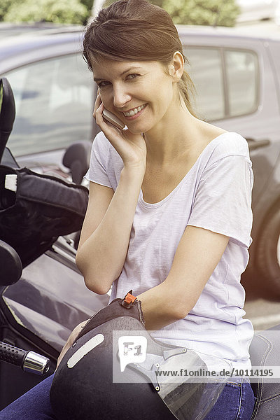 Frau sitzt auf einem geparkten Motorrad und redet mit dem Handy.