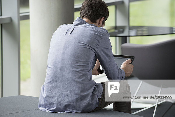 Mann allein sitzend  Blick auf digitales Tablett  Rückansicht