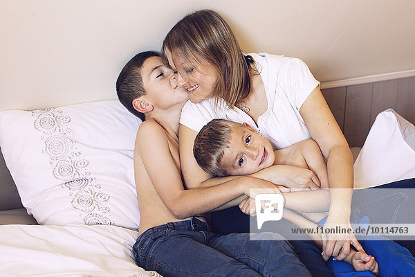 Mother and young sons relaxing together on bed