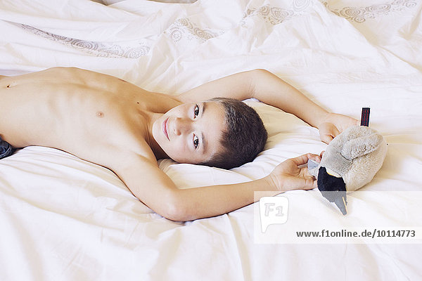 Boy lying on bed with stuffed penguin  portrait