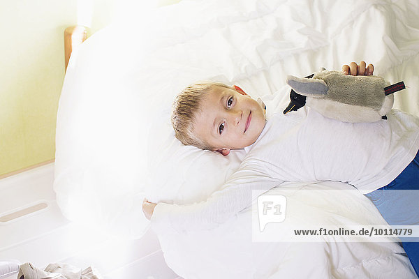 Boy lying on bed with stuffed penguin