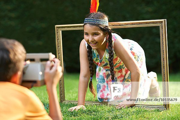 Girl kneeling  looking through picture frame  having photograph taken