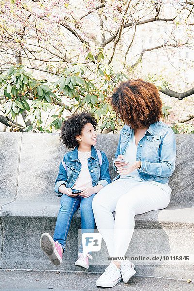 Mutter und Tochter sitzen Seite an Seite und halten Smartphones von Angesicht zu Angesicht.