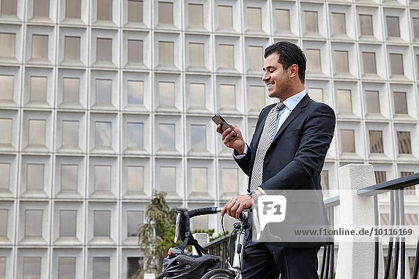 Mid adult business man holding bicycle  looking at smartphone  smiling