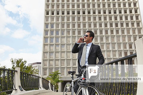 Mid adult business man holding bicycle  making telephone call using smartphone  wearing sunglasses