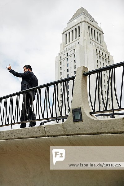 Seitenansicht des Geschäftsmannes auf dem Gehweg  Hand erhoben  Los Angeles City Hall  Kalifornien  USA