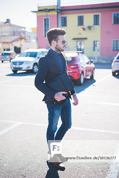 Junger Mann mit Aktentasche beim Überqueren des Parkplatzes