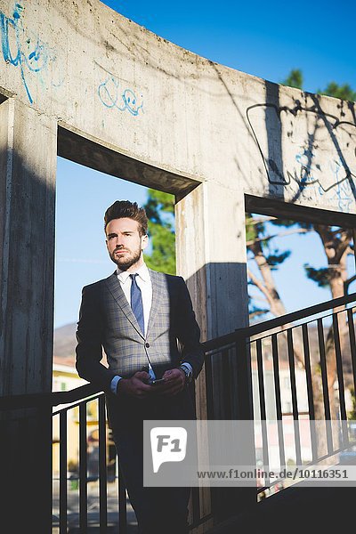 Stilvoller junger Mann mit Smartphone auf Stegstreppe