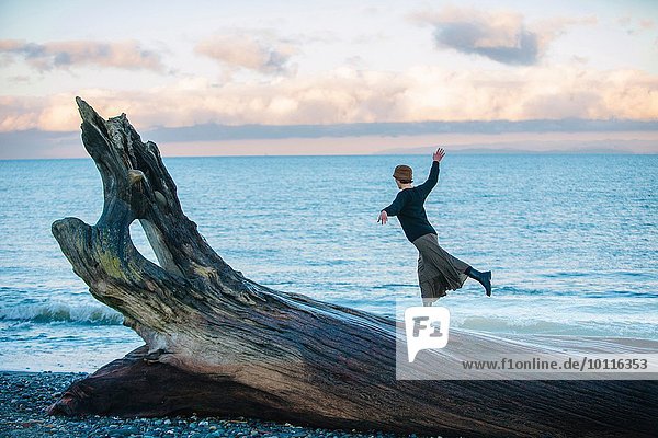 Frau auf großem Treibholzbaumstamm am Strand stehend