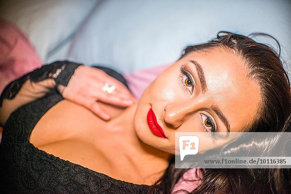 Porträt einer glamourösen jungen Frau mit rotem Lippenstift auf dem Bett liegend