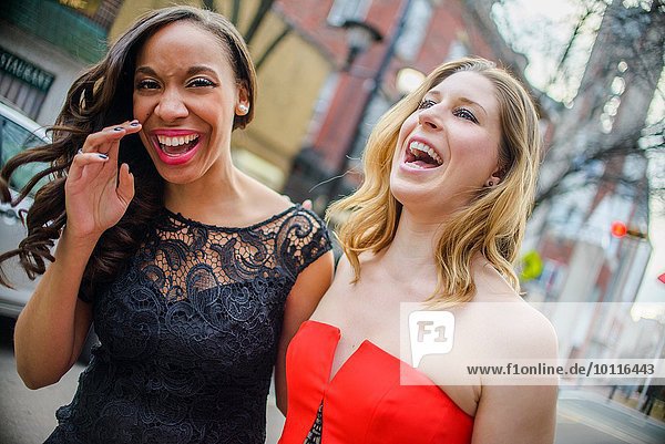 Portrait of two glamorous young adult female friends laughing on street