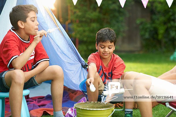 Mädchen und Brüder rösten Marshmallows vor hausgemachtem Zelt im Garten