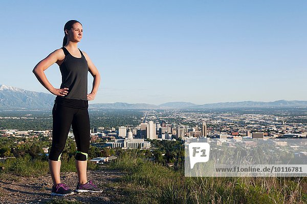 Portrait of young female runner on dirt track above city in valley