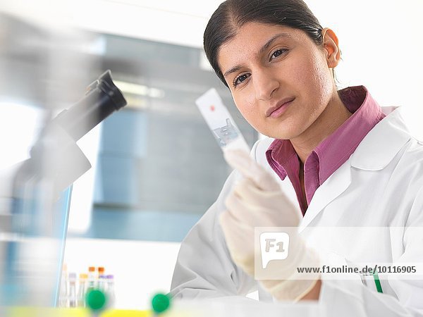 Female scientist in lab testing blood sample using microscope