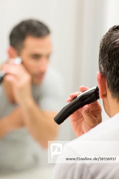 Mid adult man  looking in mirror  using electric shaver  rear view
