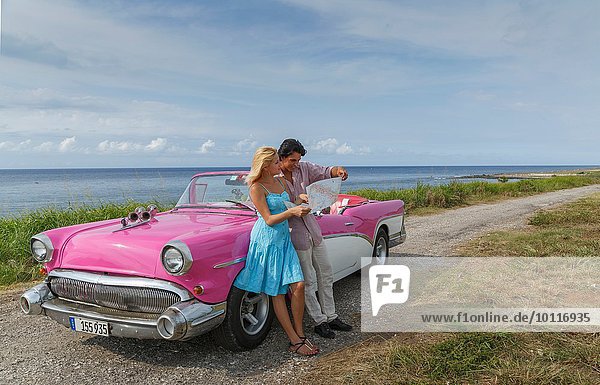 Young couple looking at map beside vintage convertible at coast  Havana  Cuba