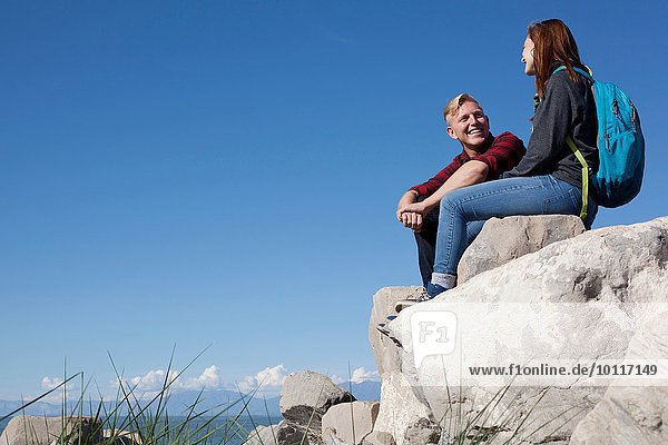 Low angle view of young couple sitting on rocks smiling