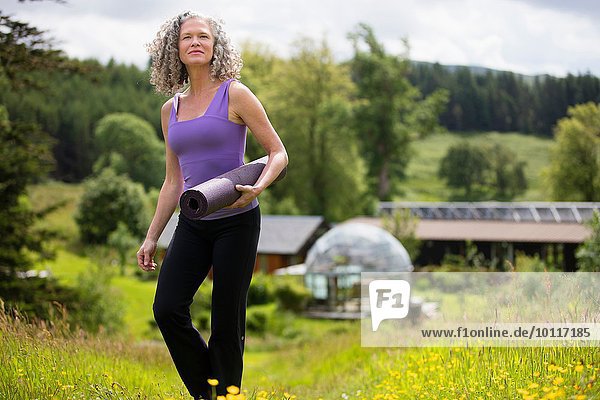 Reife Frau mit Yogamatte beim Wandern in der Öko-Lodge